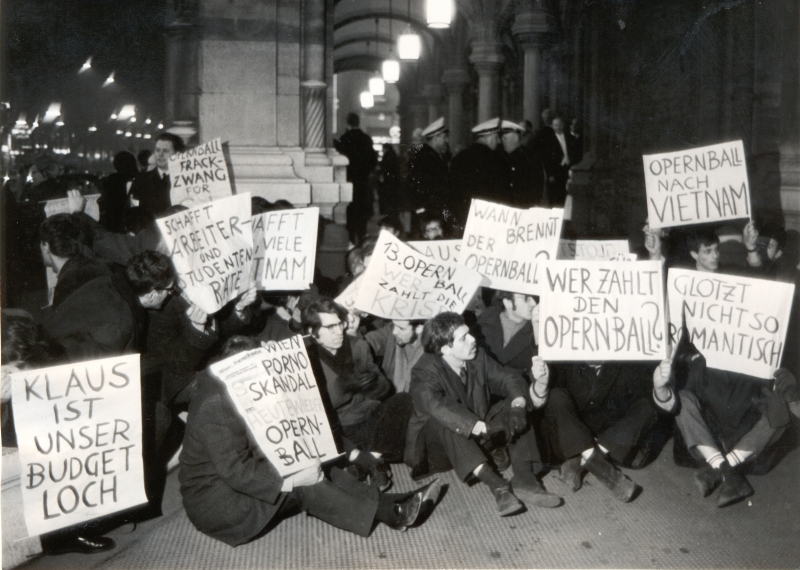 Opernball-Demonstration, 23.2.1968: Jugendliche sitzen unter den Arkaden des Operneingangs in Wien am Boden und zeigen Tafeln mit ihren Forderungen.