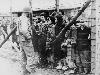 Befreite Häftlinge hinter Stacheldraht in Mauthausen (US-amerikanische Aufnahme im Mai 1945)